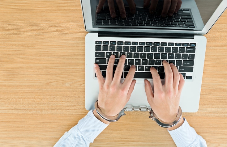 Businessman hands tied with handcuffs on laptop keyboard.