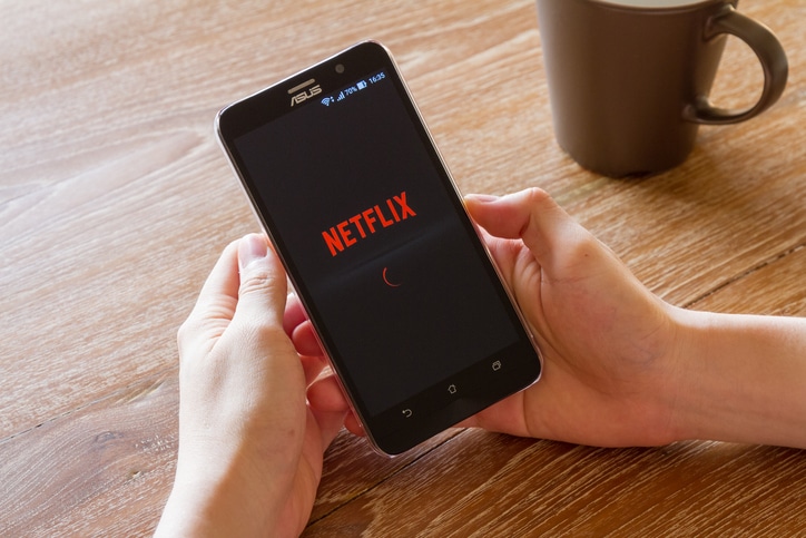 man hand holding screen shot of Netflix application showing on Asus Zenfone 2 mobile phone. Netflix is a global provider of streaming movies and TV series.