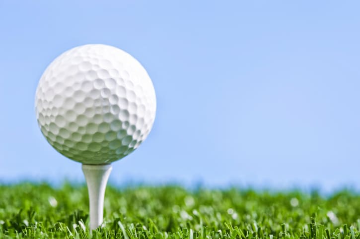 A low angle view of a Golf ball sitting on white wooden tee against a blue sky, with grass underneath