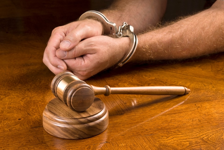 A man in handcuffs sits behind a gavel waiting for the judge to render his decision.